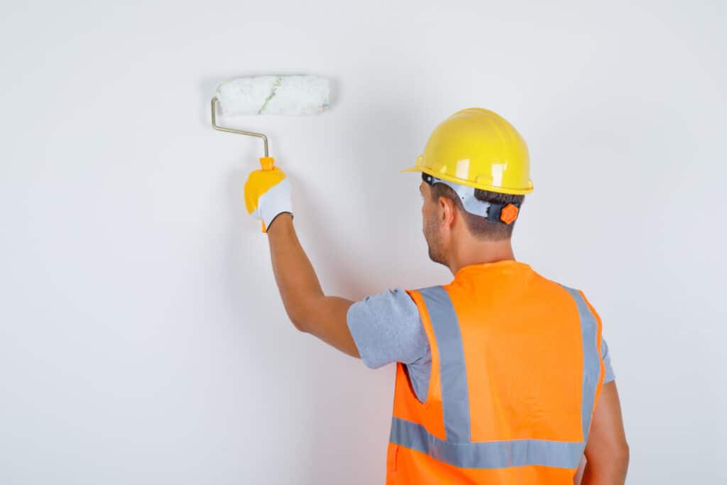 male builder uniform helmet gloves painting wall with roller back view